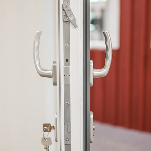 Visar handtag med nyckel på in och utsida på en vikdörr i trä. Handtagen sitter på gångdörren.